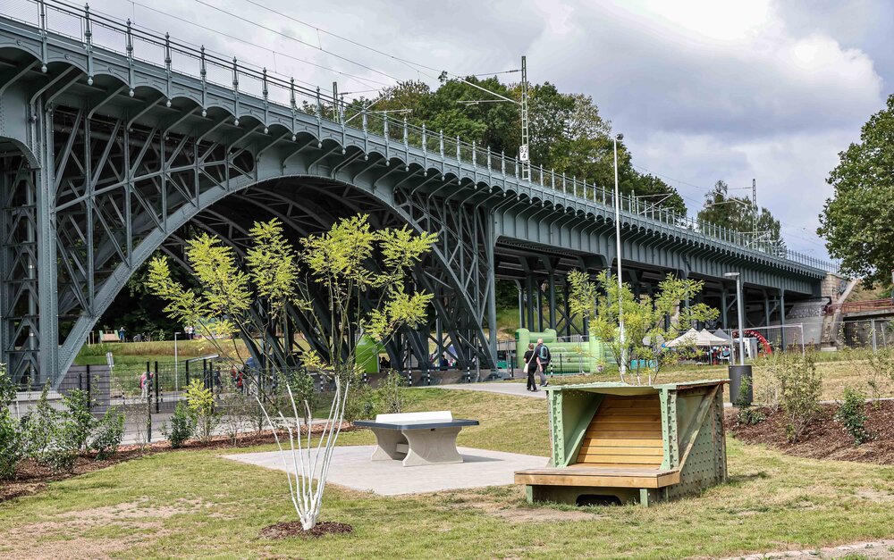 Tischtennisplatte und Sitzbank aus historischen Brückenelementen auf der Multifunktionsfläche, im Hintergrund das Eisenbahnviadukt.