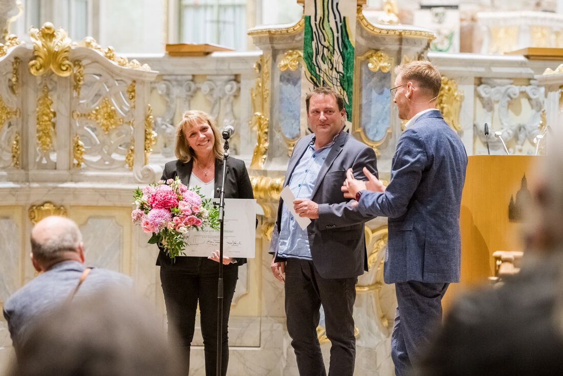 Die Preisträger halten in der festlichen Dresdner Frauenkirche ihre Urkunde und einen Bluemstrauß in der Hand.