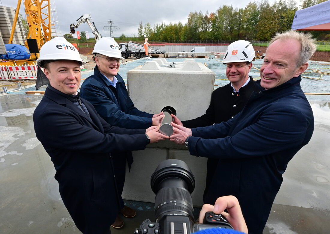 Gemeinsame Grundsteinlegung für das Kraftwerk: Die beteiligten Herrenhalten gemeinsam eine Zeitkapsel in einem Betonfundament auf der Baustelle.
