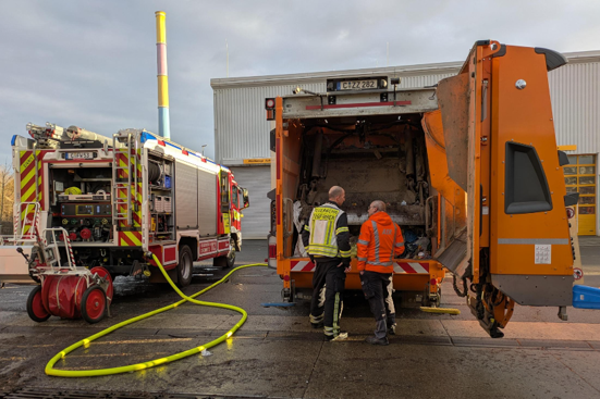 Two staff members are standing in front of a refuse collection lorry fitted with a new self-extinguishing system designed to combat vehicle fires.