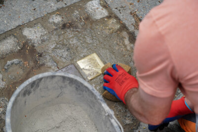 Ein Bauarbeiter verlegt den Stolperstein im Boden, befestigt ihn und wischt zum Abschluss mit einem Schwamm darüber.