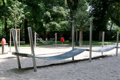 Spielgerät Hängebrücke aus Gummi über einem Kiesbett, eingerahmt von hohen Bäumen auf dem Lessingplatz in Chemnitz.