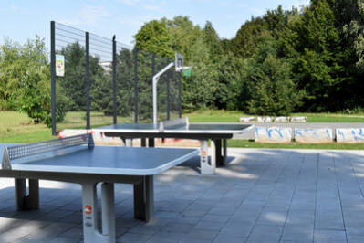 Zwei Tischtennisplatten, dahinter ein Streetball-Platz.