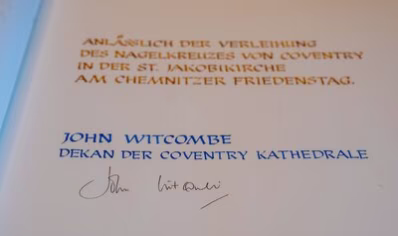 Das Bild zeigt den Eintrag in das Goldene Buch der Stadt Chemnitz von The Very Reverend Dean John Witcombe, Vorsteher der Coventry Gemeinde. Der Text lautet "Anlässlich der Verleihung des Nagelkreuzes von Coventry in der St. Jakobikirche am Chemnitzer Friedenstag".