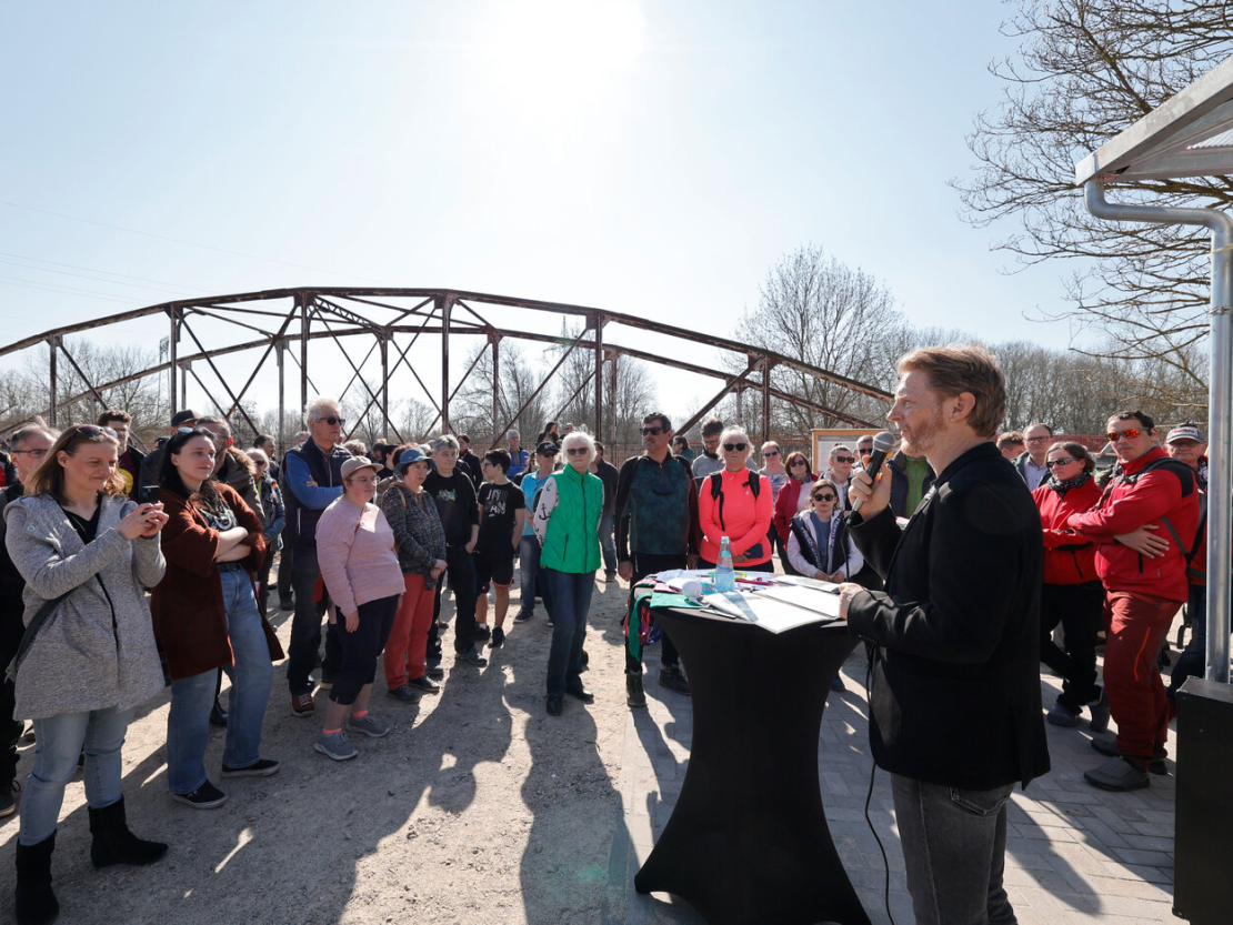 Baubürgermeister Michael Stötzer bei der Einweihung vor historischer Brücke, Zuhörer im Hintergrund.