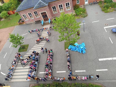 Kinder der Rudolfschule, die auf dem Schulhof ein traurigen Smiley sowie das Wort Müll darstellen