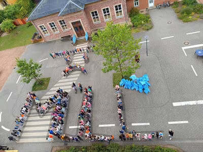Kinder der Rudolfschule, die auf dem Schulhof ein traurigen Smiley sowie das Wort Müll darstellen