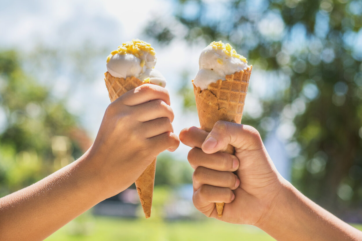 Two people are holding two waffles with scoops of ice cream aloft. These are the focal point of the picture.