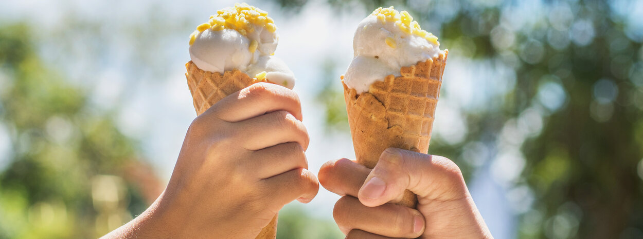 Zwei Personen halten zwei Waffeln mit Eiskugeln in die Luft. Diese stehen im Mittelpunkt des Bildes.