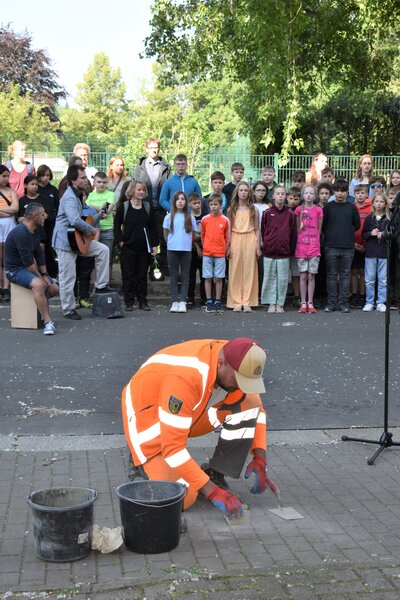 Während ein Mitarbeiter des städtischen Bauhofs den Stolperstein verlegte sangen die Schüler:innen der Montessori-Oberschule