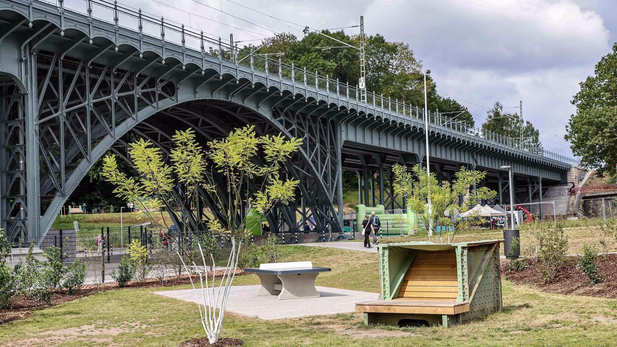 Tischtennisplatte und Sitzbank aus historischen Brückenelementen auf der Multifunktionsfläche, im Hintergrund das Eisenbahnviadukt.