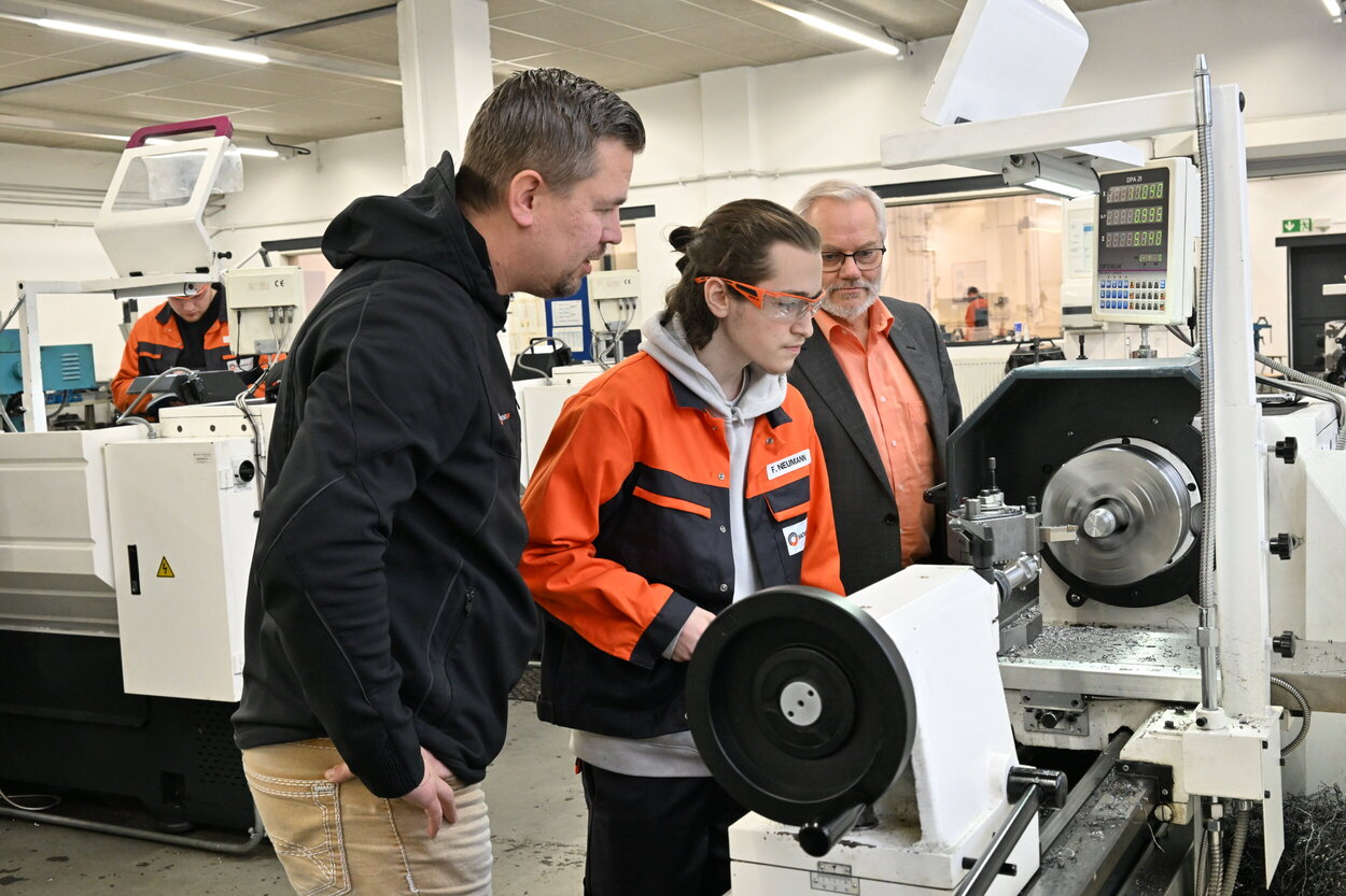 Ein Blick in die Ausbildungswerkstatt bei Sachsen Guss: Dr. Guntram Schönherr, Leiter Personal und Prokurist (r.), und Patrick Meyer, Leiter Ausbildung (vorn), schauen dem Auszubildenden Fynn Neumann an der Drehmaschine über die Schultern.
