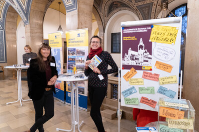 Two employees of the city administration standing next to a pinboard welcome the visitors to the meeting