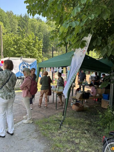 Několik lidí sbírá informace u stánku občanského sdružení Kleinolbersdorf-Altenhain pod zeleným stanem ve stínu stromu.