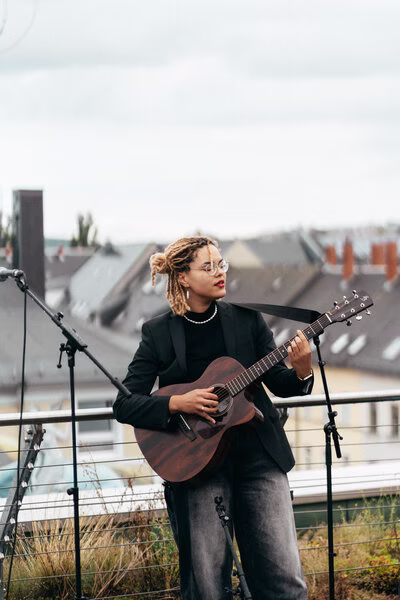 Sängerin mit Gitarre auf der Dachterrasse des Studierendenwohnheims am Brühl, dahinter Blick auf die Dächer von Chemnitz.