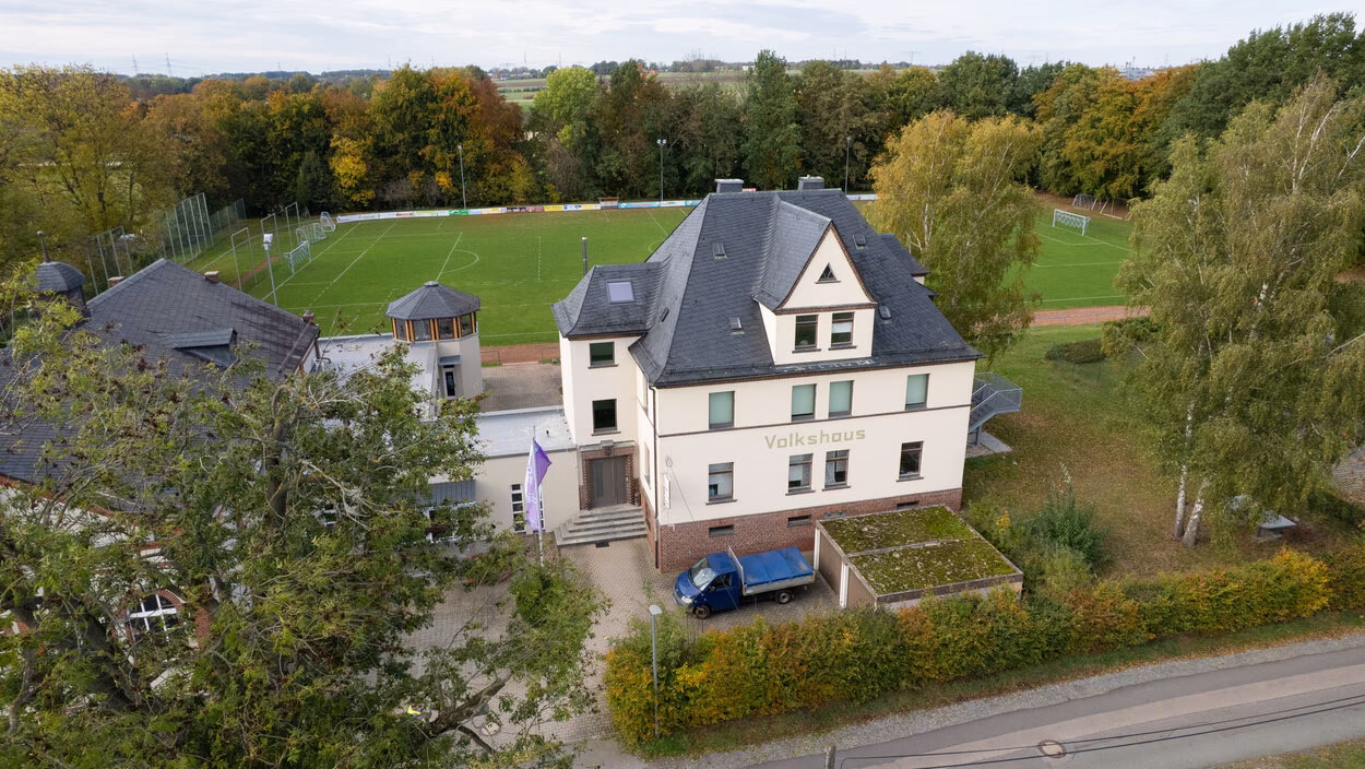 Luftaufnahme des Volkshauses Röhrsdorf mit dem dahinterliegenden Sportplatz.