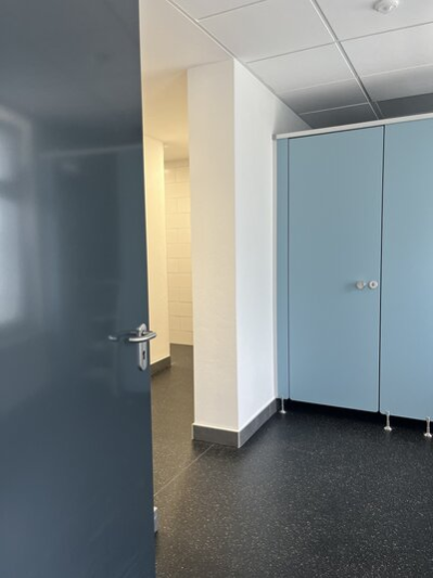 Das Bild wurde in dem sanitären Bereich aufgenommen. Es sind mehrere Toilettentüren zu sehen.