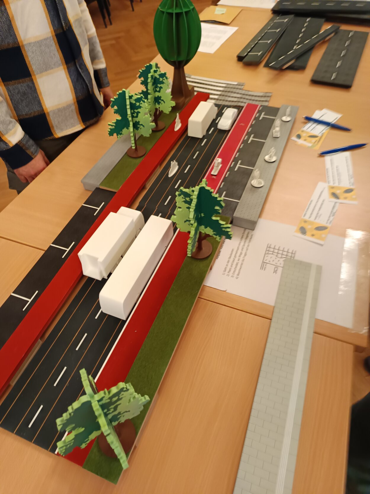 Auf einem Tisch steht ein buntes Modell von einer Straße roten Fahrradwegen, weißen Fahrzeugen und grünen Bäumen.