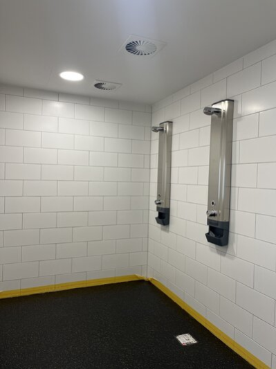 Das Bild zwigt einen Gemeinschaftsduschraum. 2 Duschen sind an der Wand befestigt.