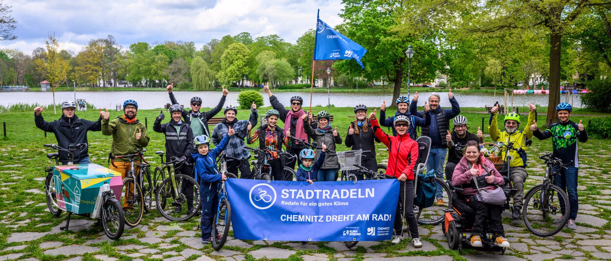 Radelnde vor dem Schloßteich halten ein STADTRADELN-Transparent sowie eine Fahne hoch