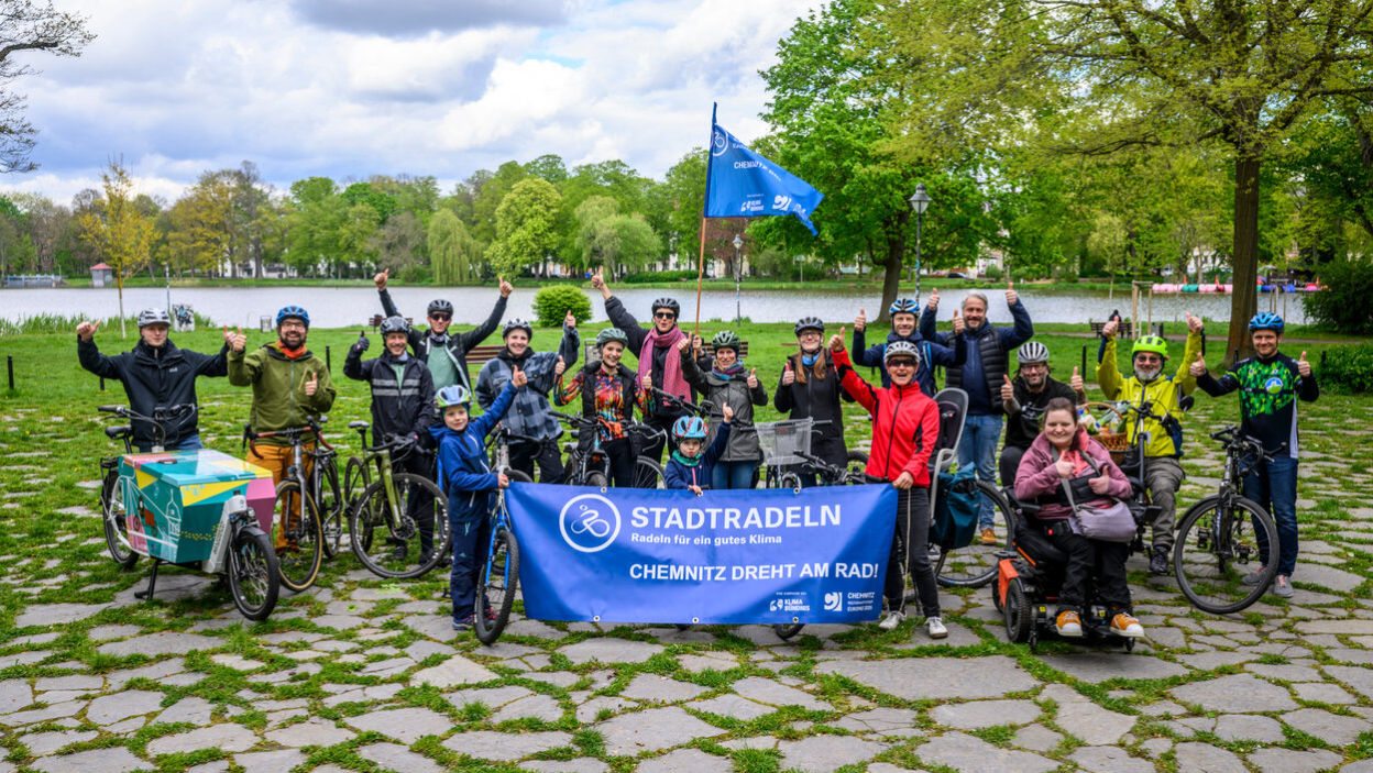 Radelnde vor dem Schloßteich halten ein STADTRADELN-Transparent sowie eine Fahne hoch
