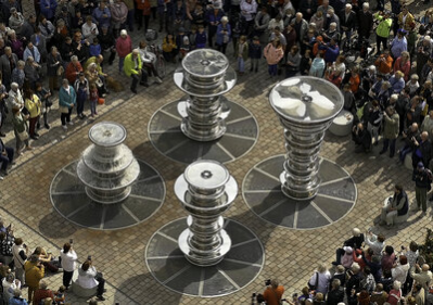Der Marktbrunnen mit vier silbernen, übermannshohen Spindeln, umgeben von Menschen.