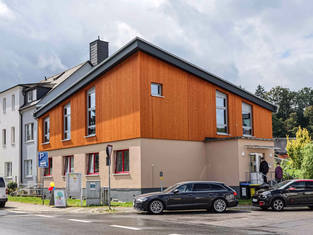 Außenansicht des Jugendclubs in Einsiedel, Erdgeschoss mit pastellfarbenem Mauerwerk, erstes Obergeschoss in orangefarbener Holztafelbauweise.