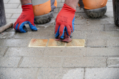 Ein Bauarbeiter hat die Stolpersteine im Boden verlegt und wischt sie abschließend mit einem sauberen Tuch ab.