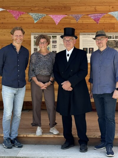 Při otevření okružní turistické stezky stojí v turistické chatě společně starosta Stötzer, Corina Krug, Jürgen Leistner ve fraku a cylindru a místní starosta Marco Gerlach.