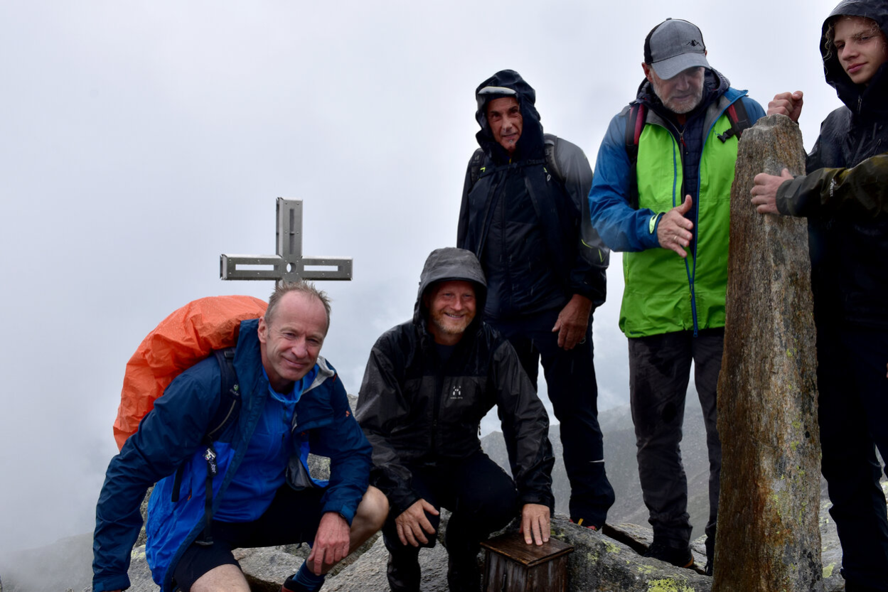 Das Bild zeigt mehrere Personen vor dem Gipfelkreuz. Alle Tragen Regenfeste Wanderkleidung. Die beiden linken Personen hocken. Die linke Person ist Bürgermeister Knut Kunze. Die Person rechts neben ihm ist Bürgermeister Michael Stötzer. Alle Personen schauen freundlich in die Kamera. Im Hintergrund ist nur grauer Nebel zu erkennen.