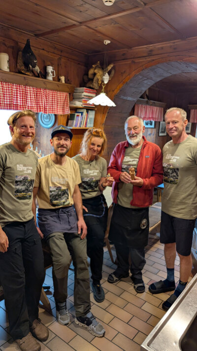 Das Foto zeigt 5 Personen, welche nebeneinander an einem Tisch stehen und freundlich in die Kamera lächeln. Das Foto wurde im Innenraum der Chemnitzer Hütte aufgenommen. Rechts steht Bürgermeister Michael Stötzer. Rechts steht Bürgermeister Knut Kunze. Zwischen beiden Bürgermeistern stehen weitere 3 Personen. 2 von ihnen halten die übergebenen Geschenke von Bürgermeister Knut Kunze und Bürgermeister Michael Stötzer in der Hand. Die beiden Bürgermeister brachten eine Statue von Karl-Marx-Monument und einen kleinen Engel mit. Im Hintergrund erkennt man den rustikalen Innenraum der Chemnitzer Hütte, welcher mit Holz verkleidet ist.