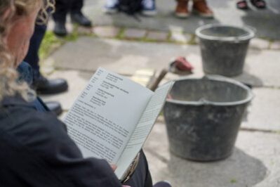 Eine Frau hält die Broschüre der Stolpersteinverlegung in der Hand.