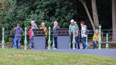 Gäste stehen am historischen Geländer des neu angelegten Aussichtsbalkons unterhalb des Eisenbahnviadukts und lesen die Informationstafeln.