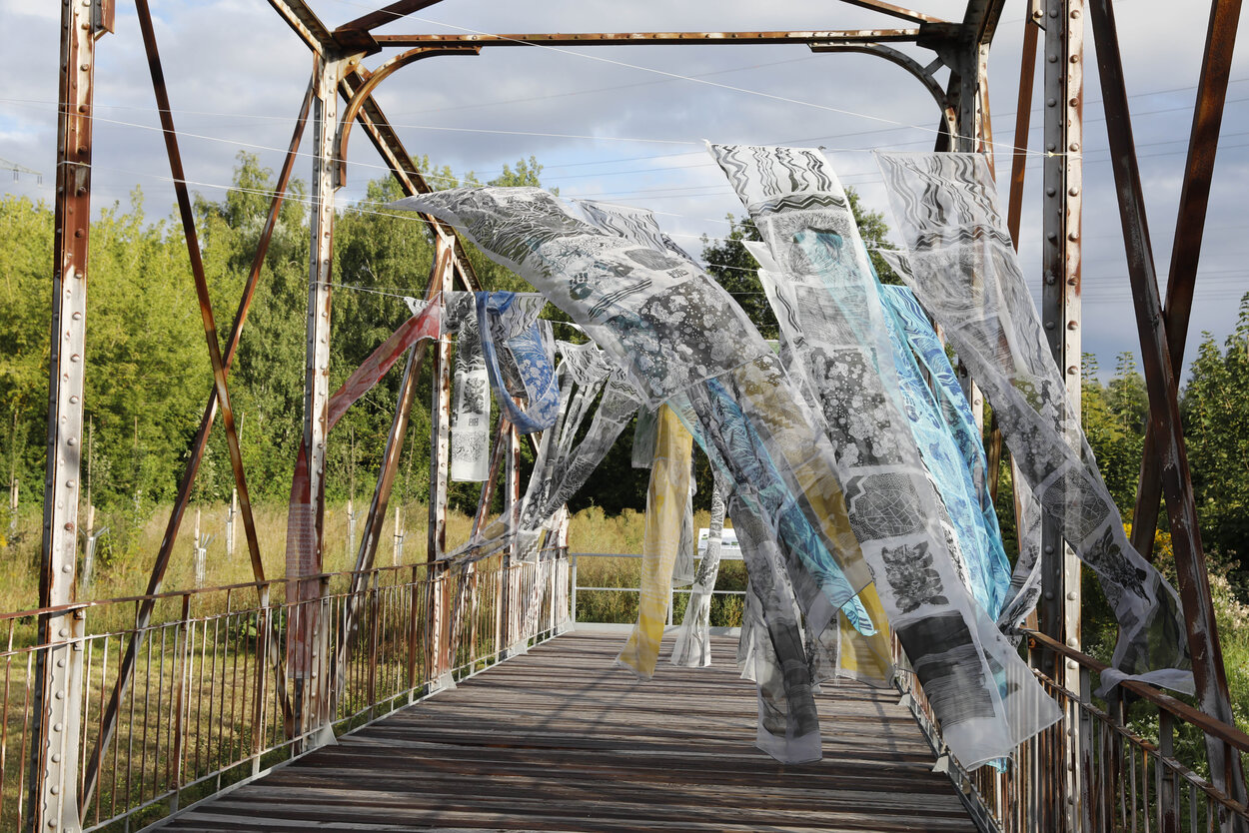 Historische Brücke mit bunten Stoffbahnen, die im Rahmen einer Kunstaktion im Wind wehen.