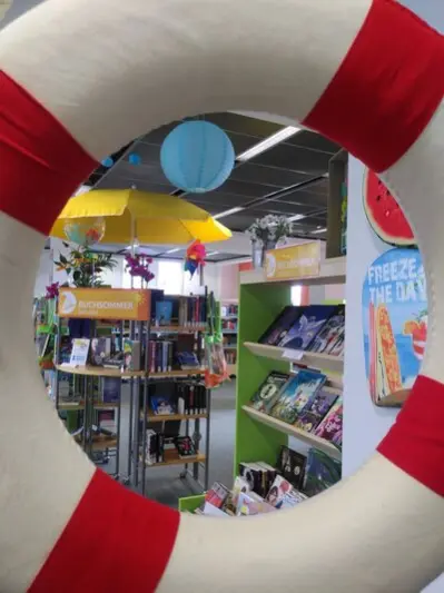 Durch einen rot/wei&szlig;en Rettungs-Schwimmring sind Regale mit B&uuml;chern die Kinderbibliothek im TIETZ zu sehen