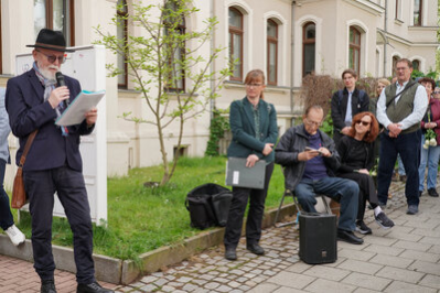 Dr. Nitsche hält eine Rede, während Carolin Guttman und weitere Besucherinnen und Besucher ihm gespannt zuhören.