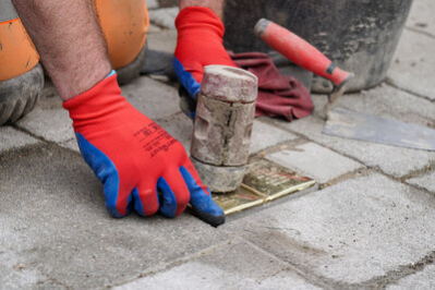 Stolpersteine werden in den Boden verlegt; ein Bauarbeiter schlägt sie mit einem Gummihammer fest in den Boden ein.