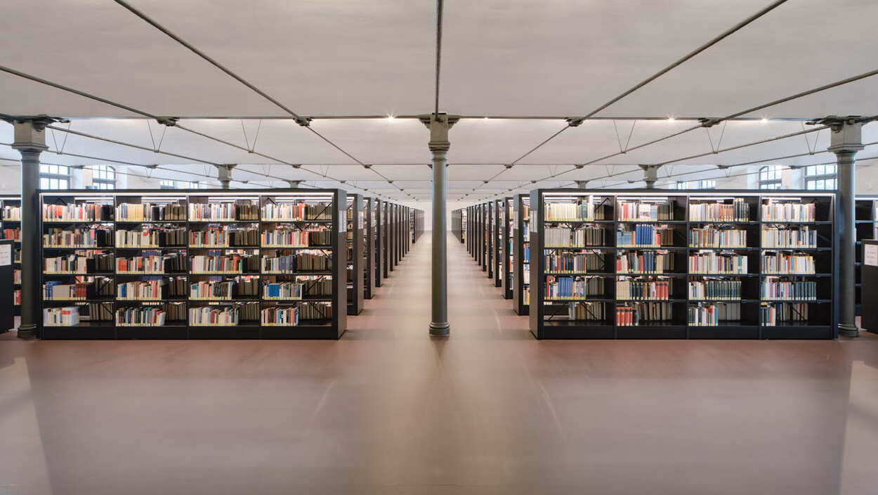 A glimpse inside the library at Chemnitz University of Technology: tall black bookshelves arranged symmetrically form long aisles, spanned by a light-coloured ceiling and slender supporting columns.