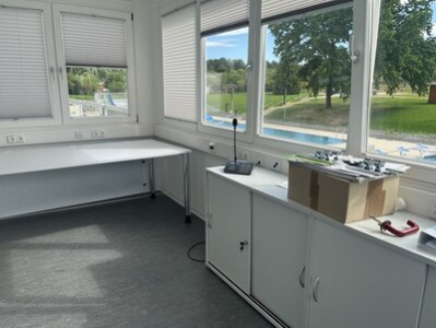 Das Bild zeigt den Raum für die Badeaufsicht. Aus den Fenstern hat man einen guten Blcik auf den Schwimmbereich. Im Raum steht ein Tisch und ein Schrank, sowie einige Gegenstände.
