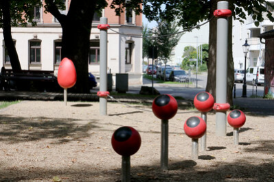 Fünf rote Kugeln mit schwarzen Punkten auf Säulen als Spielobjekte, im Hintergrund weitere Spielgeräte auf dem Lessingplatz in Chemnitz.