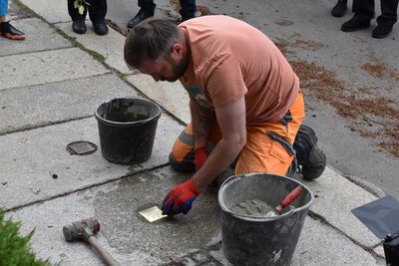 Ein Bauarbeiter verlegt den Stolperstein und reinigt ihn mit einem Tuch.