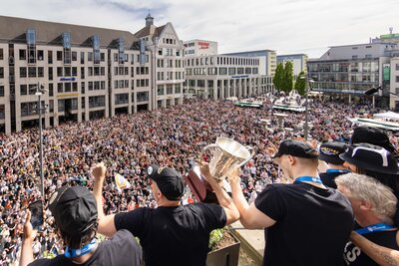 Jonas Richter, Kapitän der Niners Chemnitz, und Trainer Rodrigo Pastore stehen auf dem Rathausbalkon und präsentieren den Fans den Europapokal.