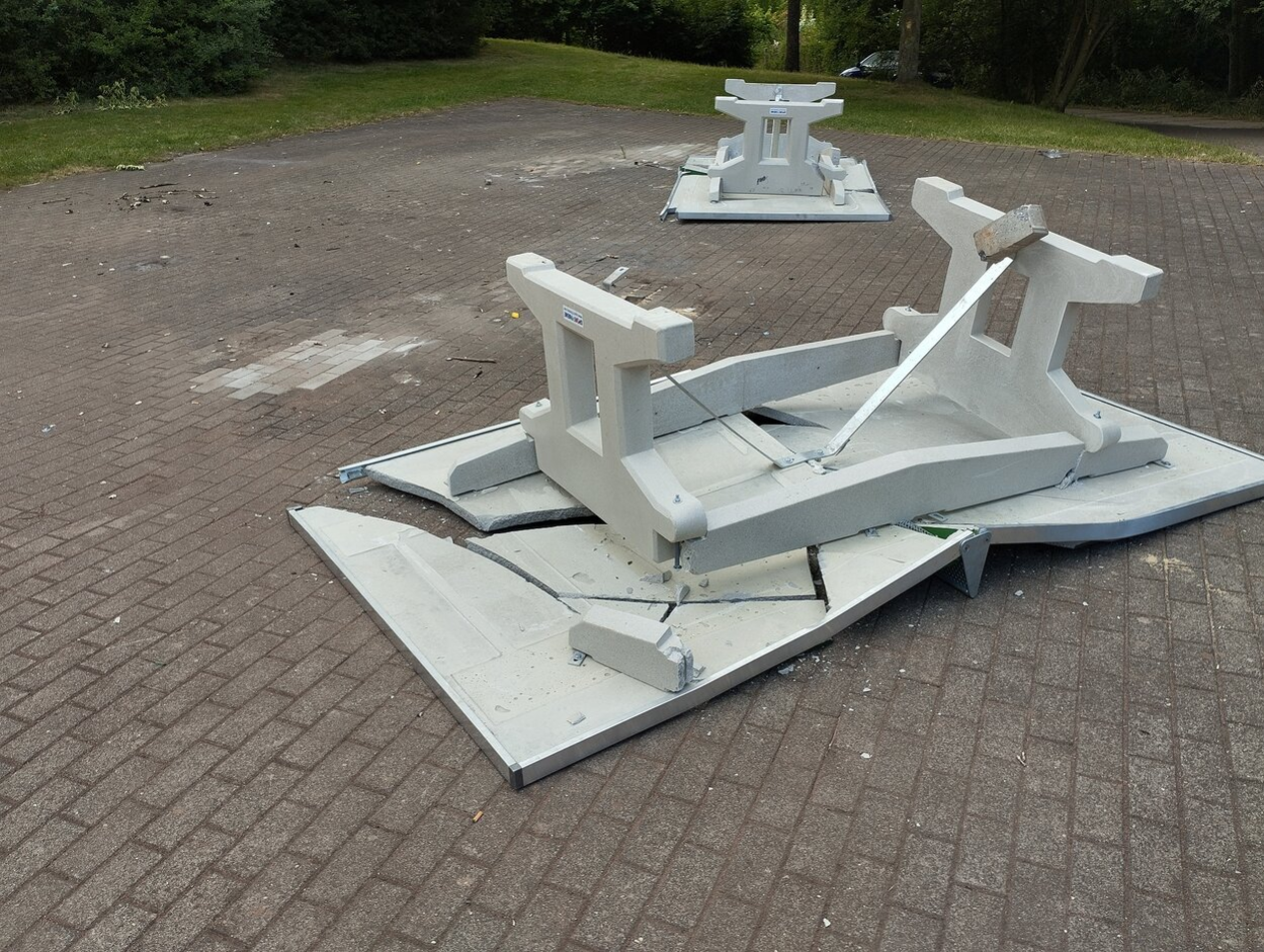 Das Bild zeigt 2 zerstörte Tischtennisplatten, welche falschherum auf einem geplasterten Boden liegen. Die Spielfläche der Betontischtennisplatten ist zersprungen.