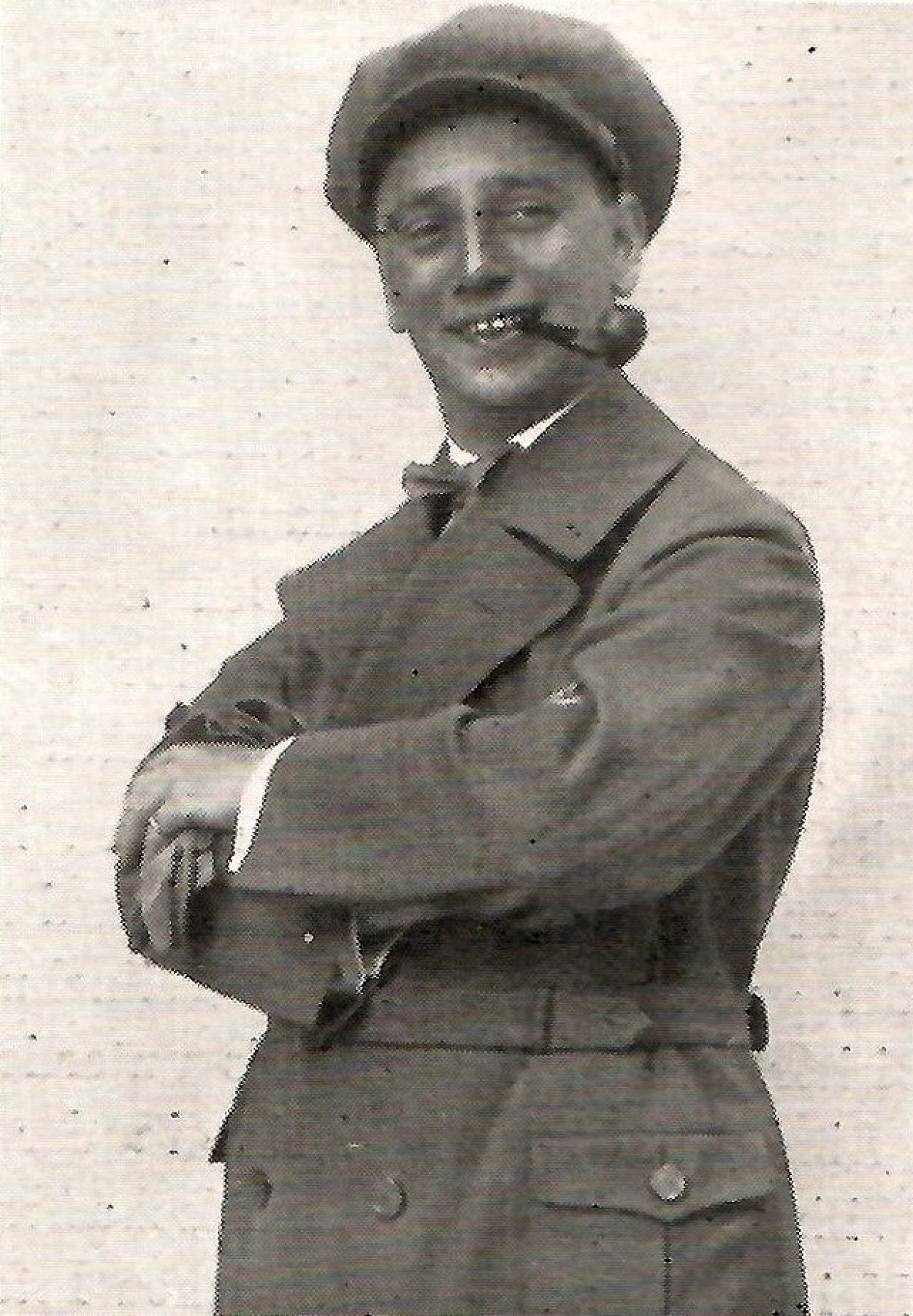 Sepia-Porträt von Erich Moral in einem Trenchcoat und Baskenmütze. Er hält die Arme verschränkt und lächelt mit einer Pfeife im Mund in die Kamera