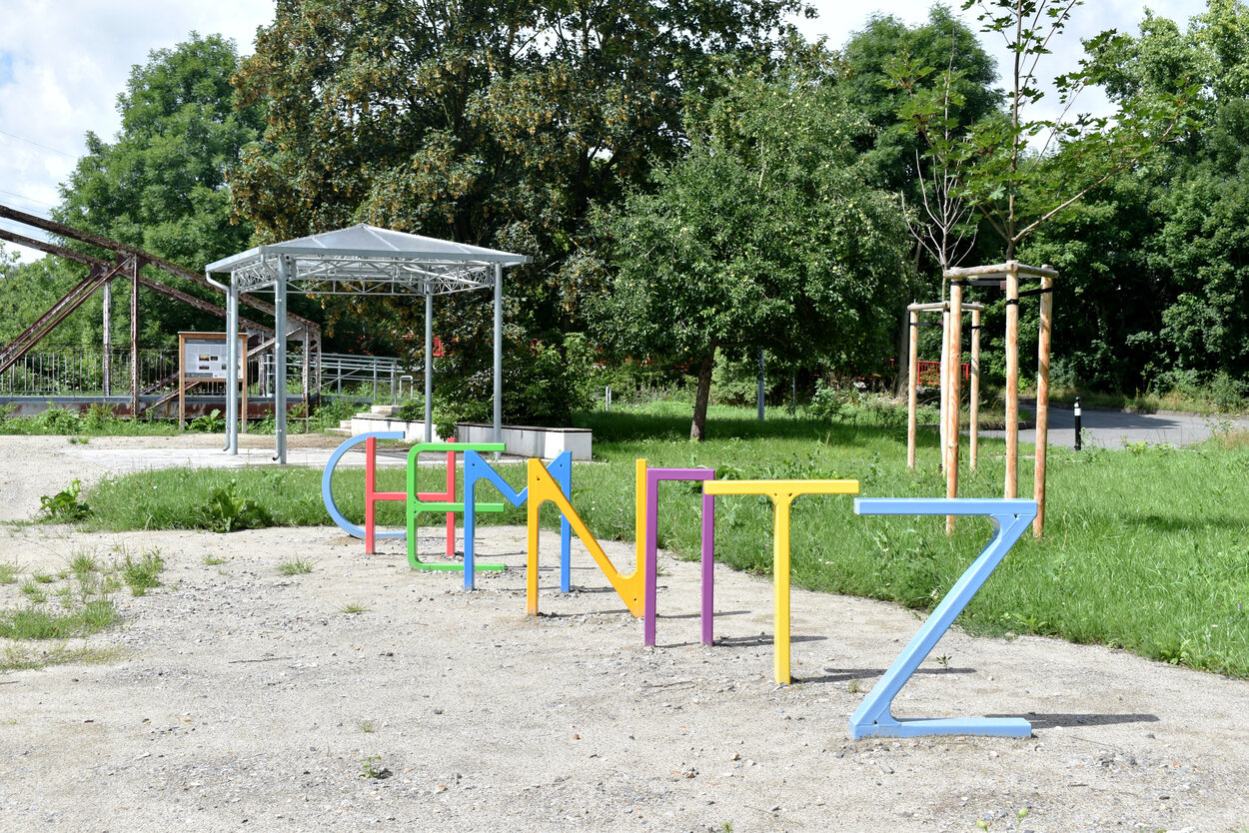 Bunte Buchstaben „CHEMNITZ“ als Fahrradständer, dahinter Pavillon.