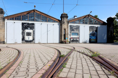 Schienen führen auf zwei Hallen zu, auf den Toren sind lebensgroße Straßenbahnen und ein Bus abgebildet.