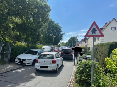 Ein weißes Auto parkt Mitten auf einem Gehweg einer Rechts-vor-Links Kreuzung.