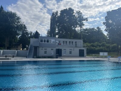 Das Bild zeigt das Bestandsgebäude für die Badeaufsicht. Bor dem Gebäude sieht man das 50 Meter Schwimmbecken.