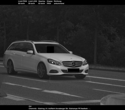 Ein weißes Auto ist in einem schwarz-weiß Bild auf einer Straße bei der Geschwindigkeitsüberschreitung zu sehen.
