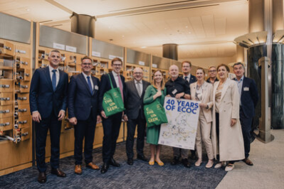 Eine Gruppe von 11 Frauen und Männern präsentiert das Plakat mit der Aufschrift "40 Years of ECOC". Ein Mann und eine Frau tragen jeweils einen grünen Beutel mit der Aufschrift "See the unseen".